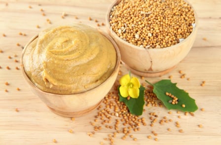 Mustard with seeds and mustard flower on wooden background