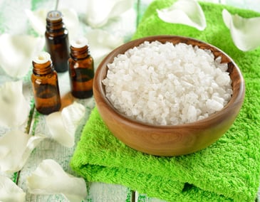 Salt in a wooden bowl and essential oil on a white table