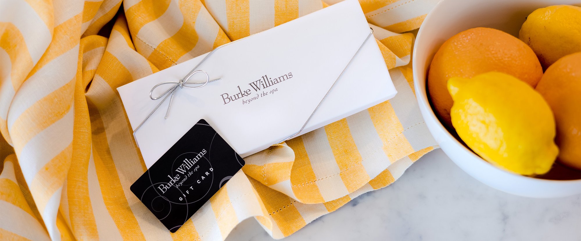 a Burke Williams gift card on a yellow striped placemat with a bowl of lemons a Burke Williams gift card on a yellow striped placemat with a bowl of lemons